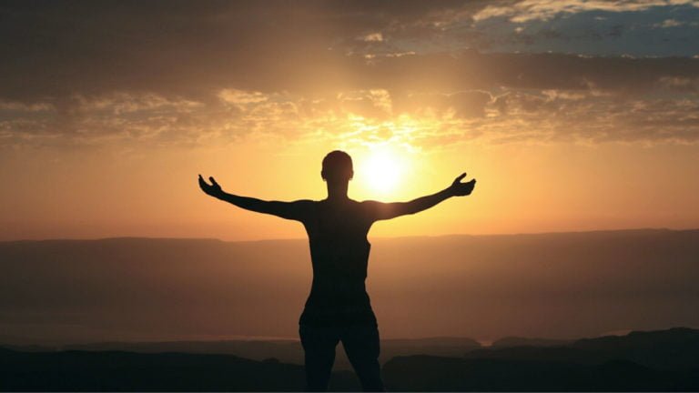 Person looking at a sunrise with arms outstretched in gratitude